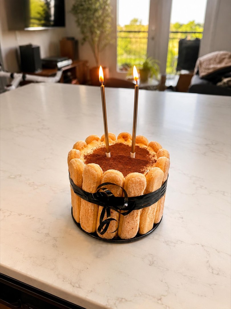 A ladyfinger-wrapped birthday cake with gold candles.
